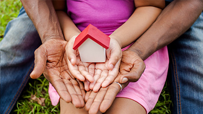 close up of two people's hands holding a wooden toy home
