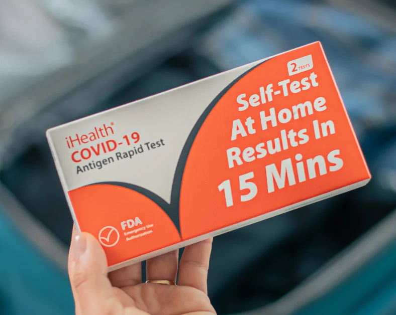 Hand holding ihealth covid test box, orange graphics on white box