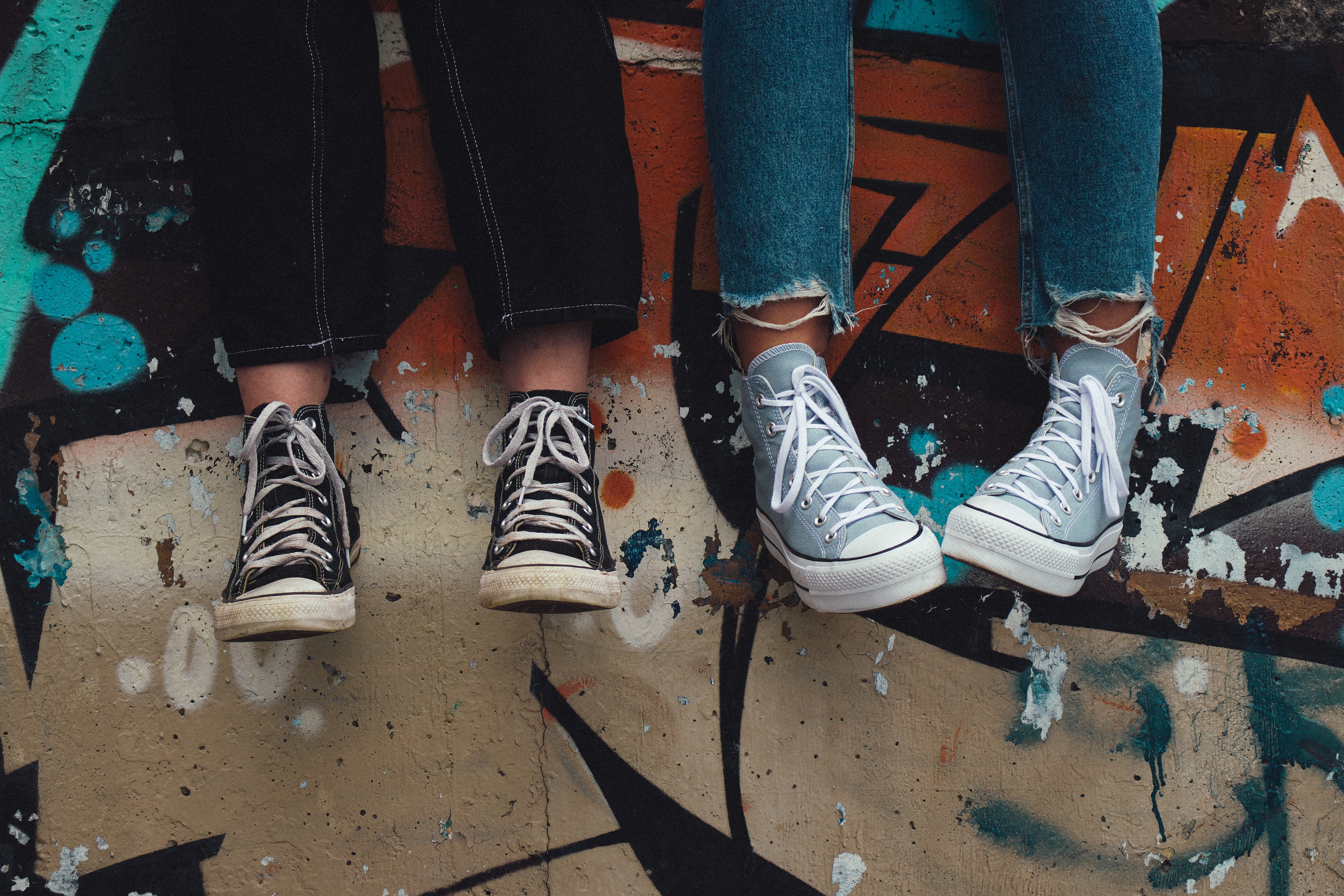 two feet in sneakers against a graffiti-covered wall