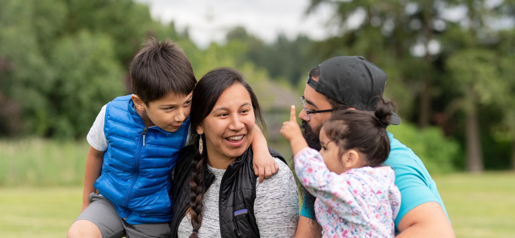 An Indigenous family smiling in the park, two young children and their parents.