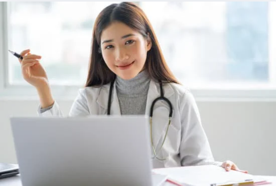 A smiling young female health care provider seated at a desk behind a computer.