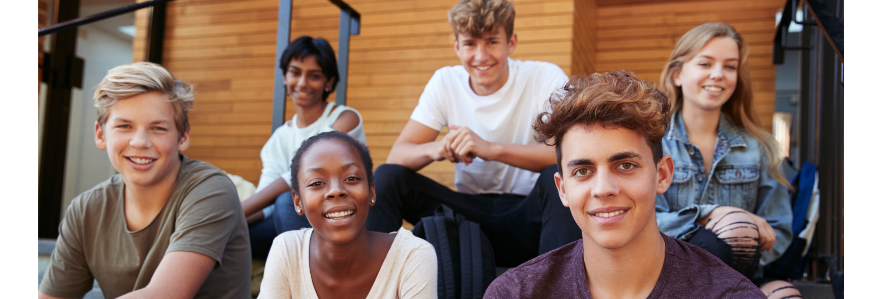 Group of six teenagers sitting on steps, smiling, and looking at the camera.