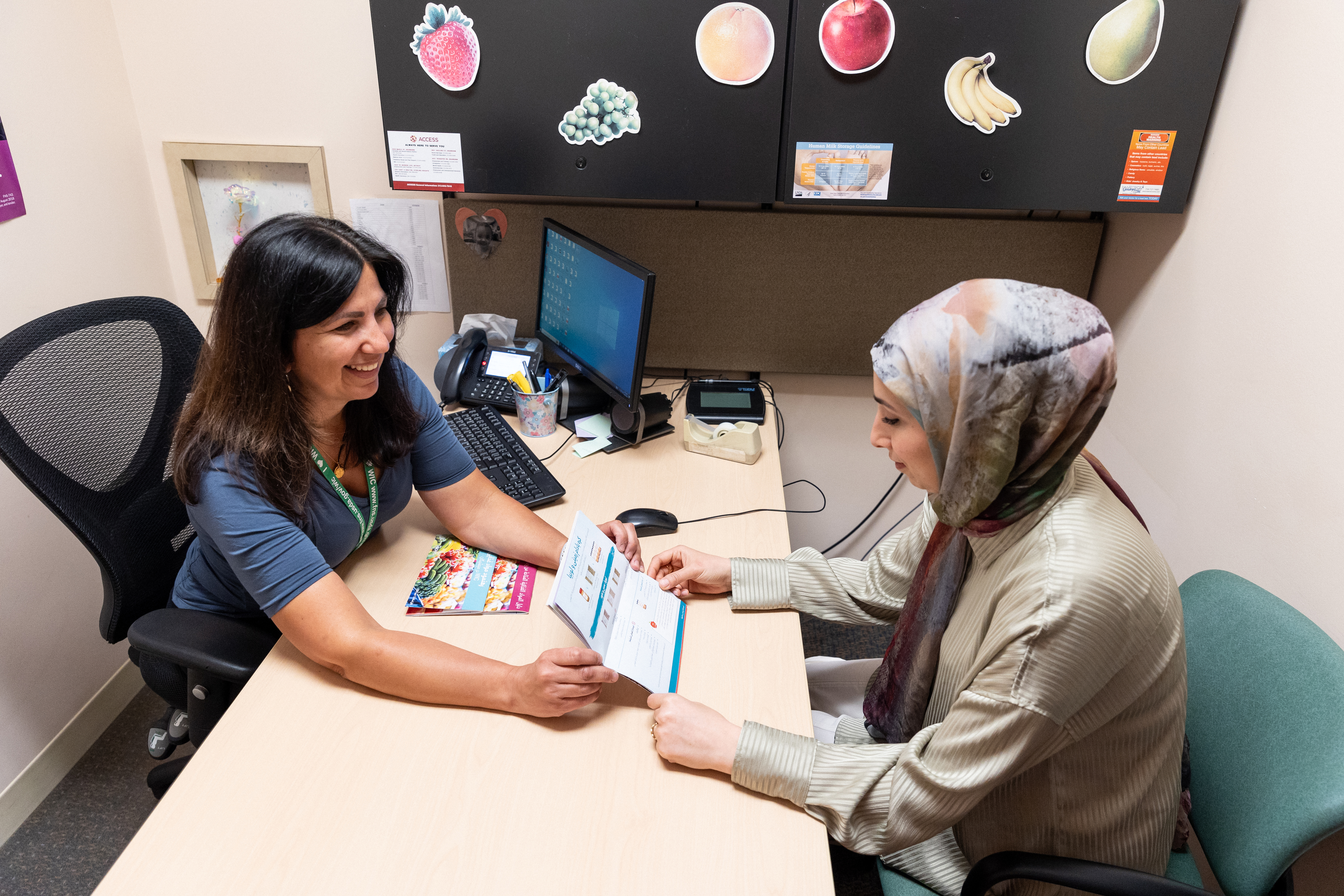 WIC staff shows a printed resource in Arabic to a participant.
