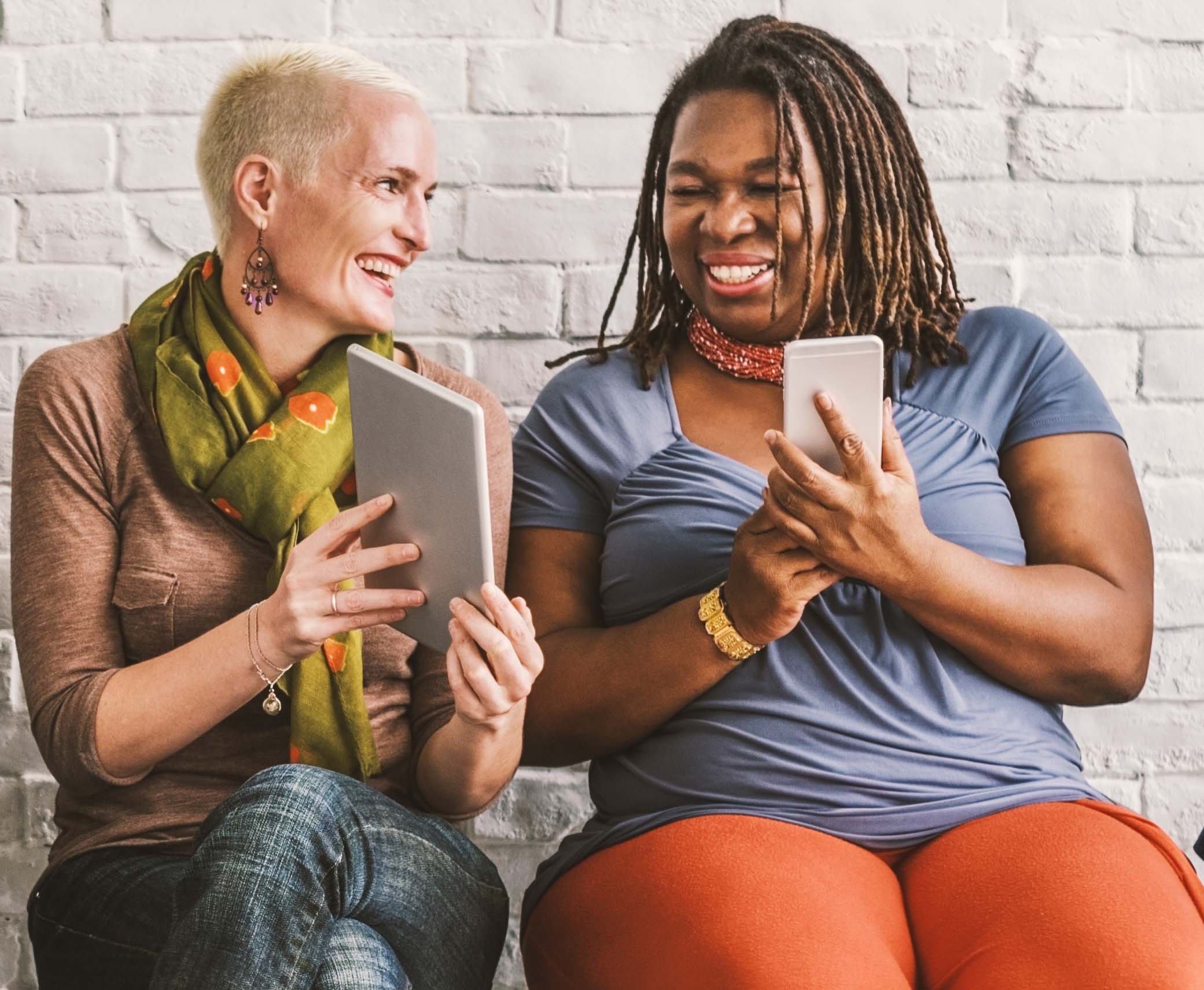 Stock photo of two women smile while showing each other their screens on handheld electronic devices