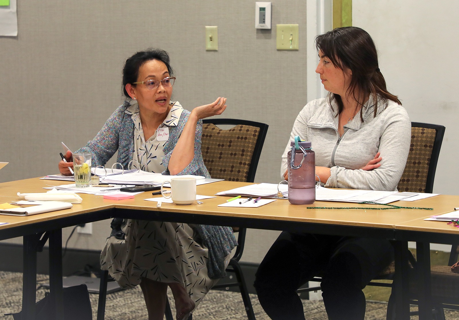 Two members of the HEZ Evaluation Team sit at a table with office materials while in discussion.