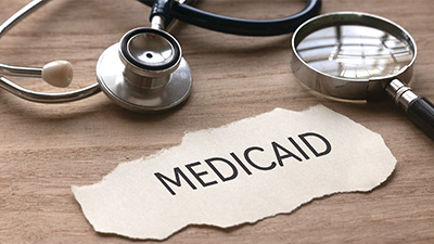 close up of a paper strip with the word Medicaid. A stethoscope and magnifying glass to the side.