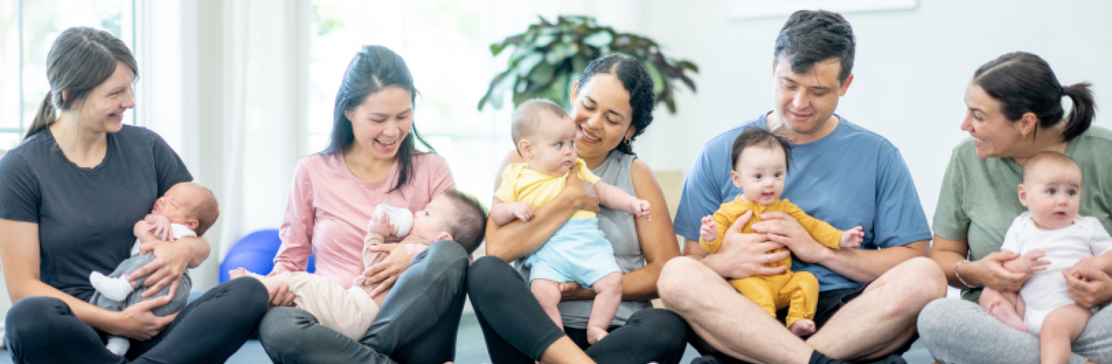 Five parents holding infants as they sit together on a floor.