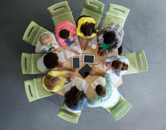 View above a table where nine diverse people are seated working together.