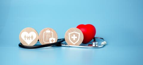 Stethoscope, small red heart, and three wood coins with healthcare icons on a blue background