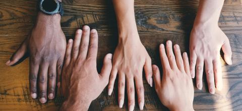 Five hands of different ethnicities and genders side by side on a wood surface. 